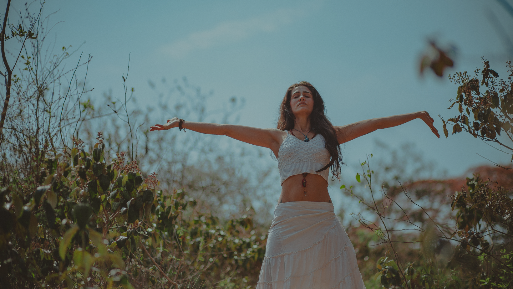 Woman in a white dress standing with arms outstretched in a natural setting